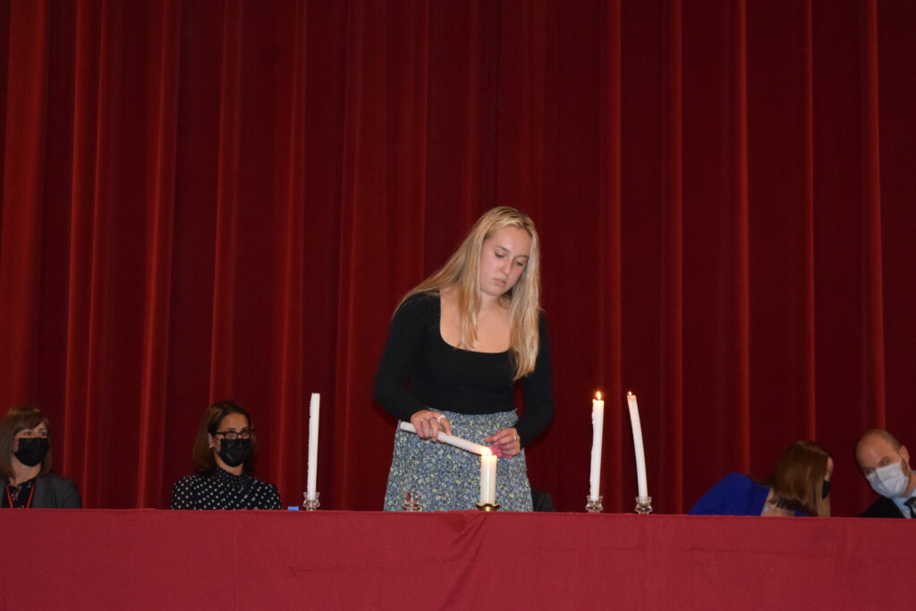 (PHOTO: Lighting the candles for the 2021 members of the National Honor Society. Hadley Bernardi lights the candle representing service.)