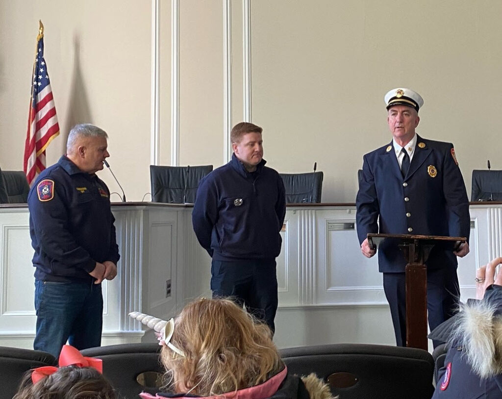 (PHOTO: New Rye Fire Fighter Andrew Wood listens to comments from Captain John McDwyer. Public Safety Commissioner Michael Kopy is at the far left. At Rye City Hall on Friday, March 4, 2022.)