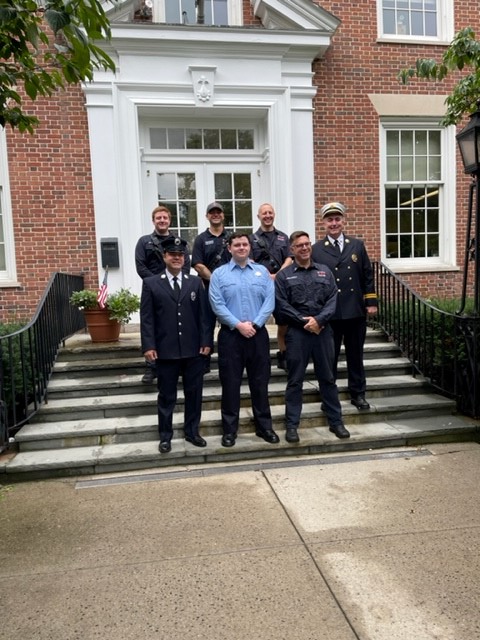 (PHOTO: Rye's newest firefighter William Junior (center, blue shirt) appears with Rye FD members in front of Rye City Hall.)