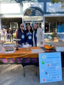 (PHOTO: Children’s Philanthropy Bake Sale volunteers: Kendall Truman, Rye Councilwoman Julie Souza, and Claudine Hanley at the 68th annual Halloween window painting in Rye.)