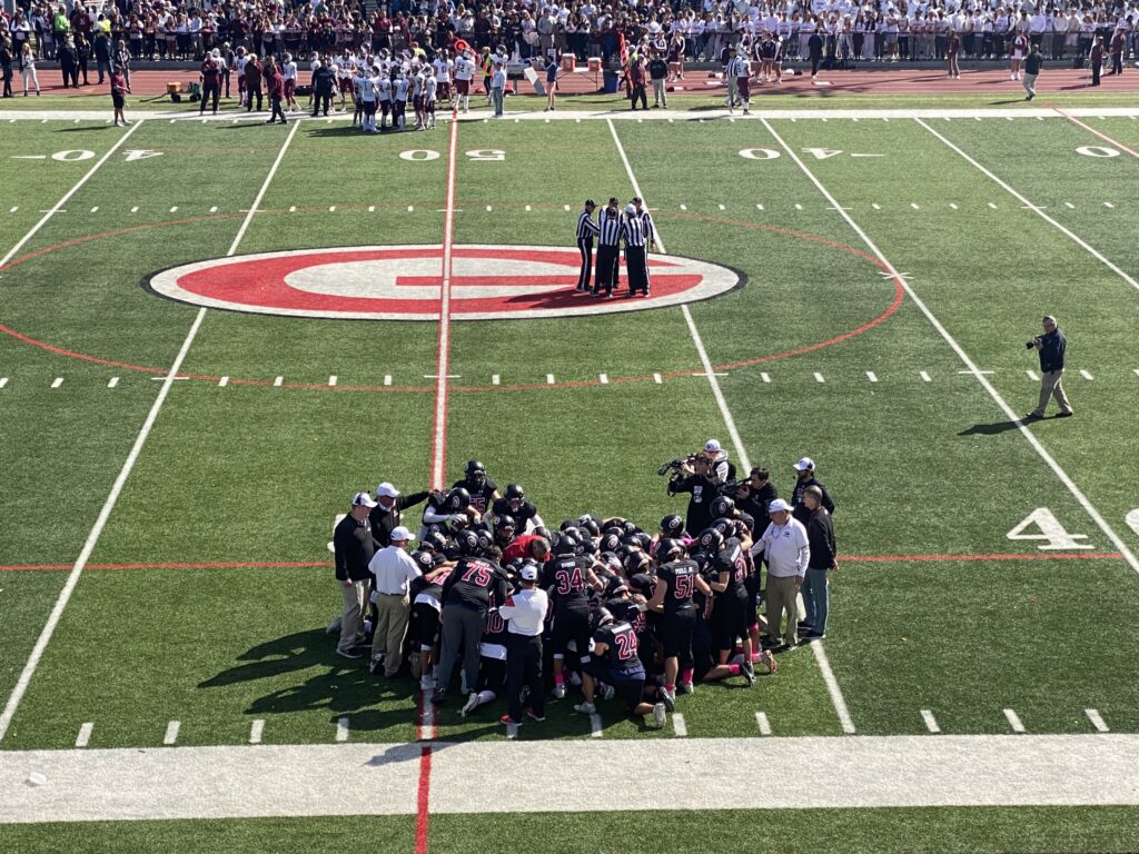 (PHOTO: Rye Varsity Football Coach Dino Garr talks to his team just before kickoff at the Rye Harrison football game on Saturday, October 8, 2022.)