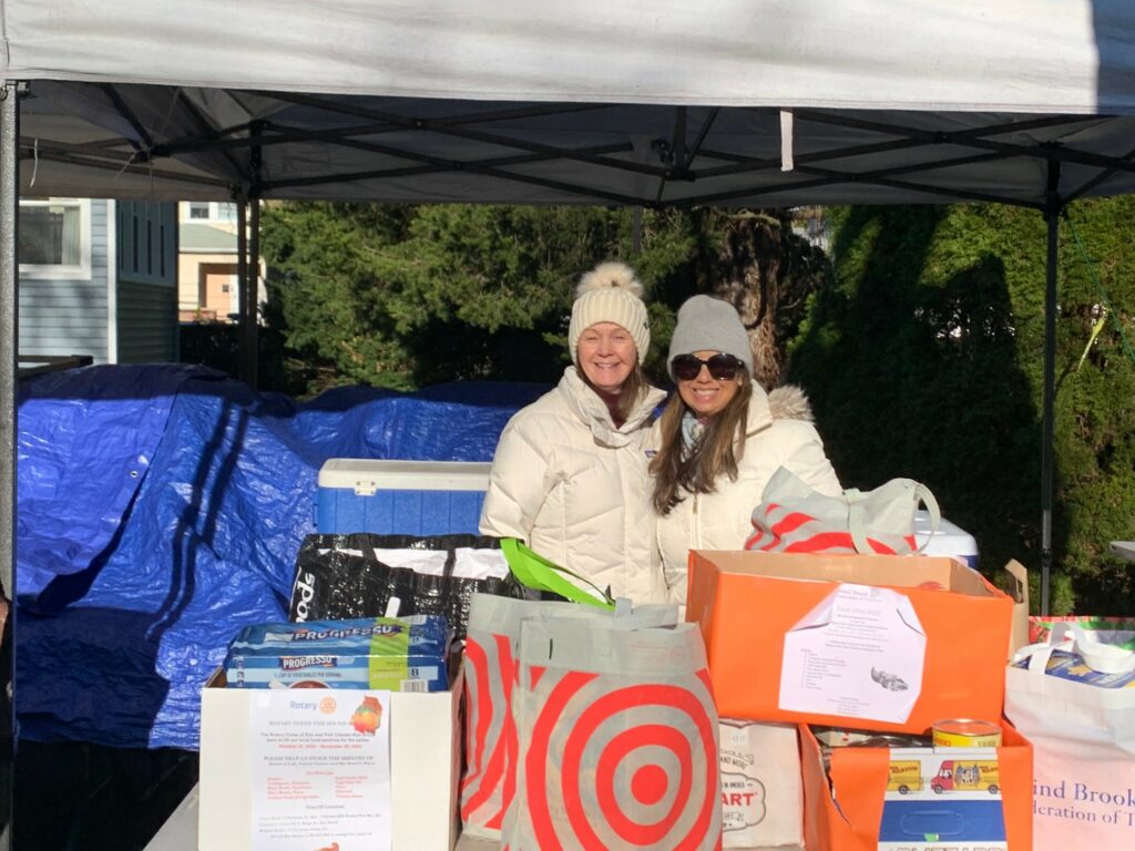 (PHOTO: Rita Tino (far right) stand in front of collection boxes on distribution day with fellow Rye Rotary member Cathy DeMartino.)