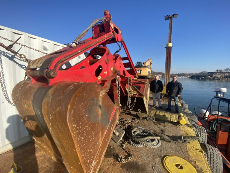 (PHOTO: Chair of the Boat Basin Commission Joe Pecora and Boat Basin Supervisor Rodrigo Paulino, CMM on the dredge barge Wednesday. A large crane shovel is on the left.)