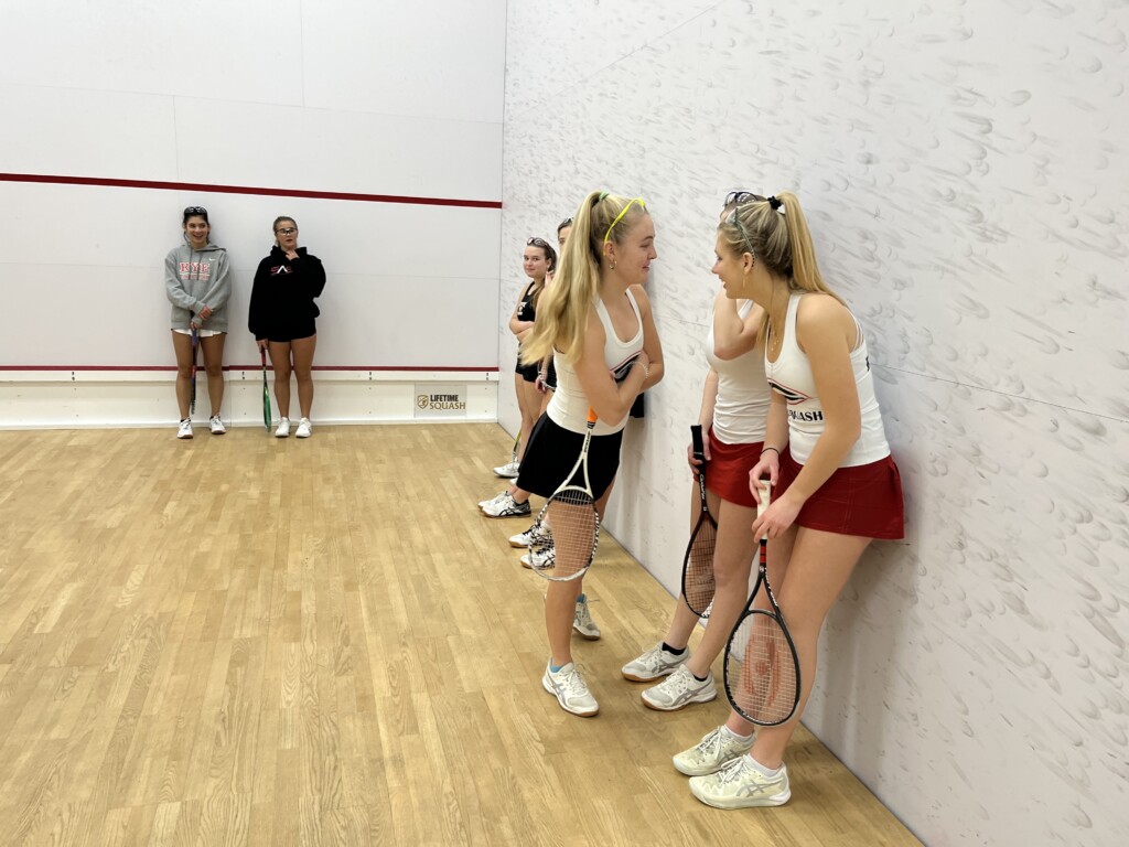 (PHOTO: Rye Girls Varsity Squash senior captains Despina Sfiris and Charlotte Langer look down the line at the team in preparation to introduce the lineup.)