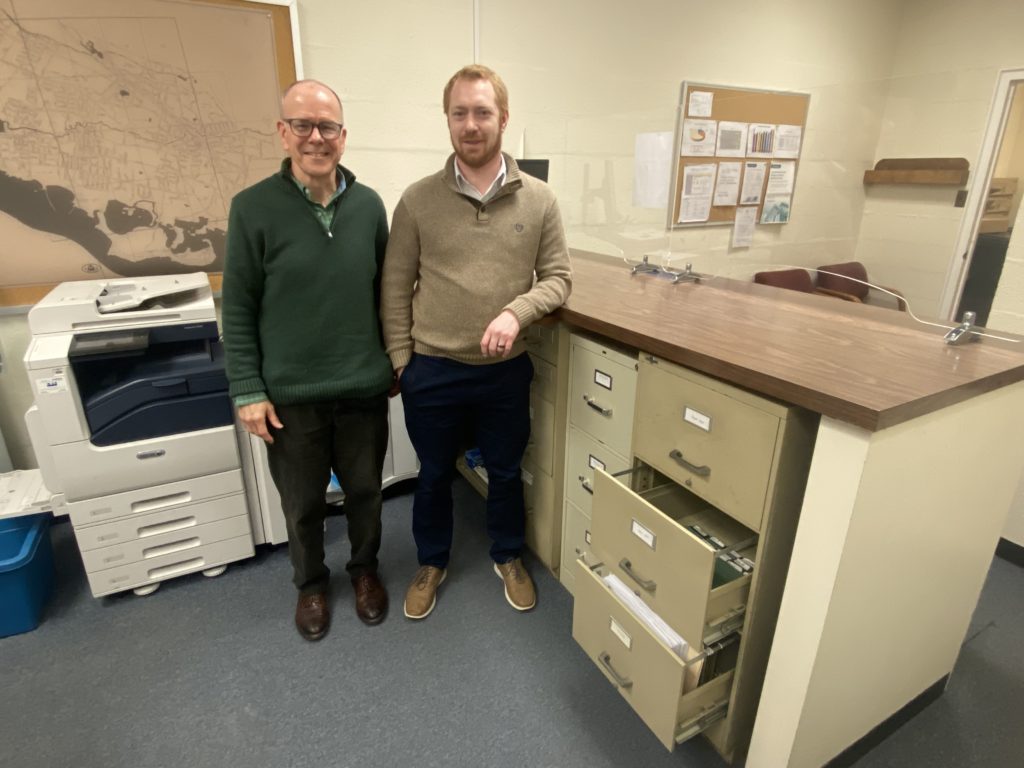 (PHOTO: Rye City Assessor Patrick McEvily and Assistant Assessor Jon Flynn standing in front of the file cabinets that typically hold the 5,200 property cards on each and every land parcel in the City of Rye.) 