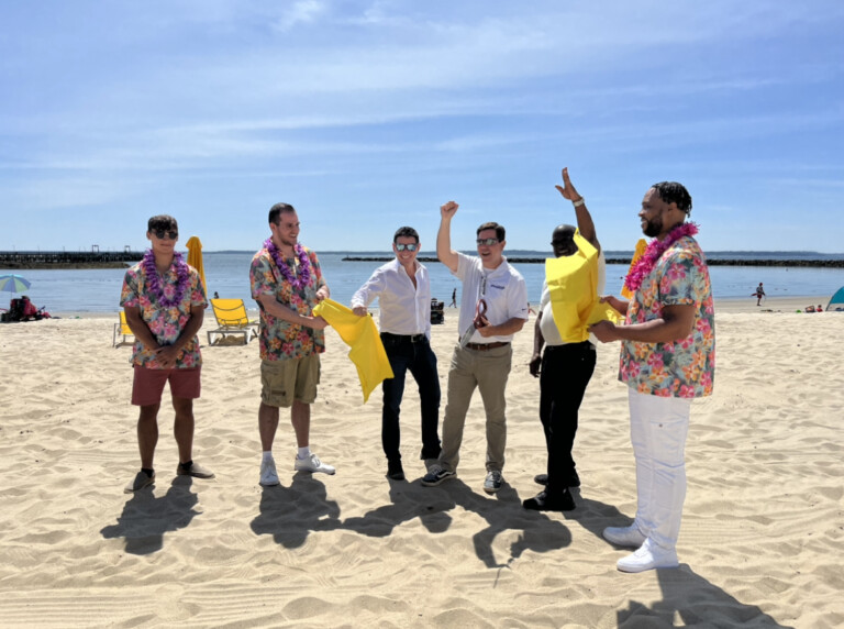 (PHOTO: Rye Playland Beach & Pool Opening May 27, 2023: Nick Singer, managing principal of Standard Amusements (the firm with the long term management contract for the park), Playland General Manager Jeff Davis and Westchester County Deputy Executive Ken Jenkins along with members of a steel drum band, cut the ribbon to welcome visitors to the newly opened and appointed beach and pool. The pool facilities have been closed since 2019 due to both COVID and a multi-million dollar pool and bathhouse renovation. Credit: Will McCullough.)