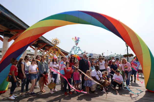(PHOTO: The Pride parade marchers gather for a photo under the rainbow arch on the Playland boardwalk on Saturday, June 10, 2023. Credit: Sierra Desai.)