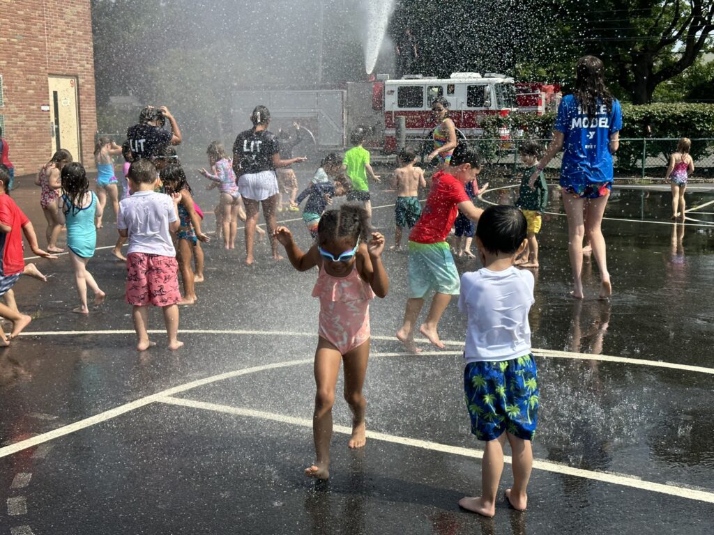 (PHOTO: On Thursday, July 20, 2023, the Rye Fire Department brought their firetruck to the Rye Y's Discovery Camp to cool down the Explorers group campers (ages 4 & 5). The camp is located at the Osborn School.)