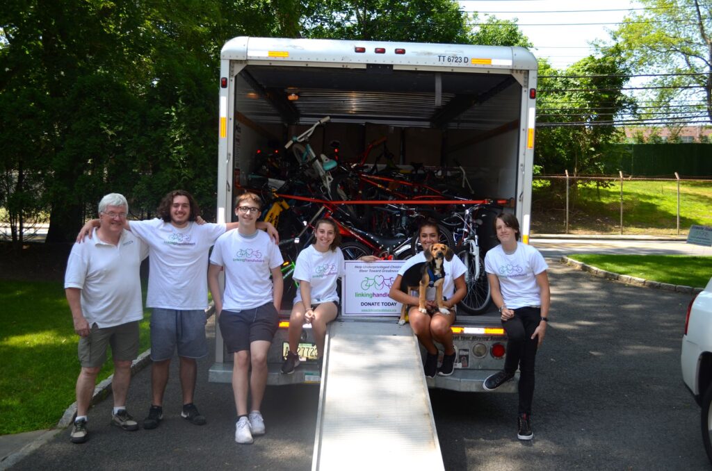 (PHOTO: Linking Handlebars loading up a U-Haul for a bike giveaway. Left to right: Kas Kasprowicz (WCC mechanic and driver), Luca Villani, Edward Lawrence, Sophie Bross, Cristiana Villani with Kaya the dog and Ben Roath.)