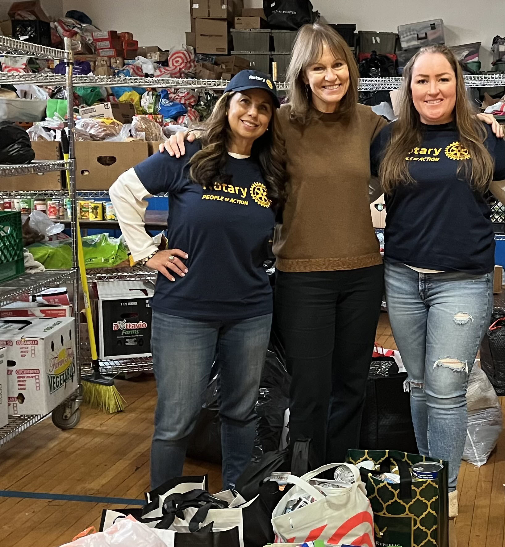 (PHOTO: Rita Tino, Esq. of Rotary Club of Rye who coordinated the 2023 annual food drive (L) is joined by Rotary Club Secretary Cathy Garr (Center) and Club President Lauren Torres next to some of the more than 1,000 pounds of food collected through this year’s drive. The items will be distributed to several food panties and other non-profits for the holidays.)