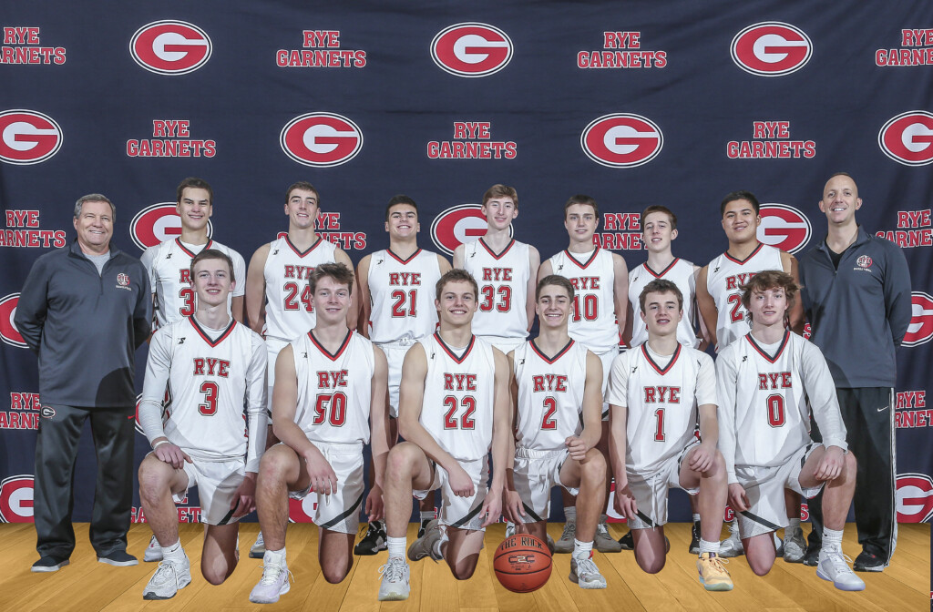 (PHOTO: The 2023-2024 Rye Boys Varsity Basketball team: standing (L to R): Assistant Coach Bart DiNardo, Charlie Rupp (34), Jake Kessner (24), Patrick McGuire (21), Jack Brennan (33), Henry Shoemaker (10), Justin McCarthy (30), Andrew Wilmarth (23), Head Coach John Aguilar. Kneeling (L to R): Charlie Margiloff (3), Charlie Stevens (50 or 5), Rocklan Boisseau (22), Carson Miller (2), Ben Hudson (1), Quinn Monaghan (0).)