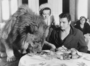 (PHOTO: Buster Crabbe, famous actor at lunch with Jack, one of his lions and partner in his film, in a Hollywood restaurant on February 6, 1933 in Hollywood, California. Credit: Unknown (Keystone-France), Public domain, via Wikimedia Commons.)