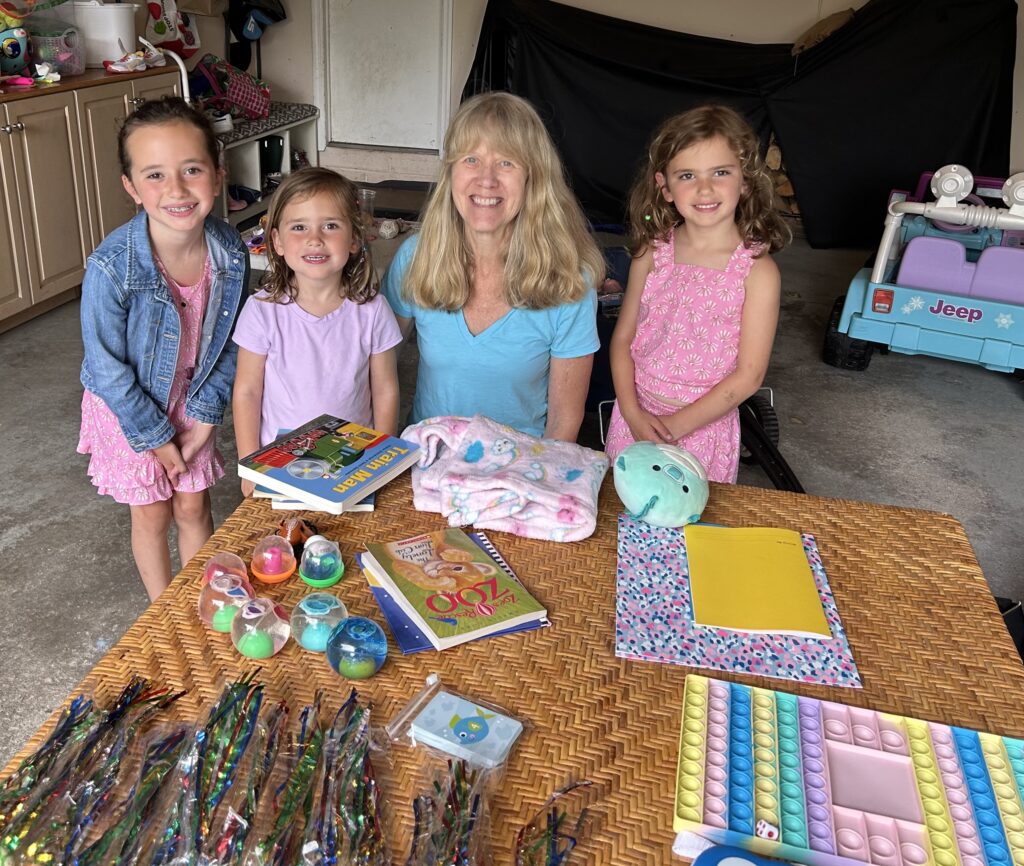 (PHOTO: Sue Wexler, director of community outreach for Bread of Life [aka Giving Tree Global] and winner of the 2023 Rye Human Rights Award winner stocking shelves with Maggie, Molly and Annie Burke who were selling their treasures to raise money for the group's food pantry work.)