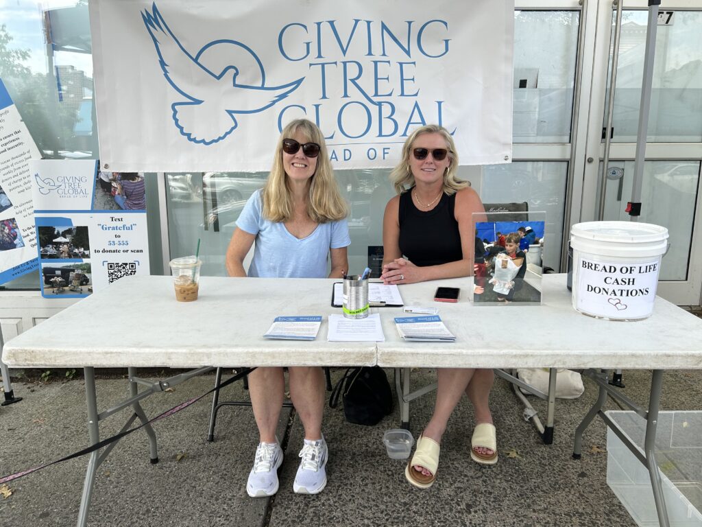 (PHOTO: Sue Wexler, director of community outreach for Bread of Life [aka Giving Tree Global] and winner of the 2023 Rye Human Rights Award winner stocking shelves with Laura Becton at a local sidewalk sale raising funds and awareness.)