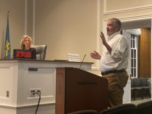 (PHOTO: Rick McCabe, chair of the Rye Recreation Commission, speaking about NUrsery Field at the March 6, 2024 Rye City Council meeting. City Clerk Noga Ruttenberg looks on from behind the three minute clock.)