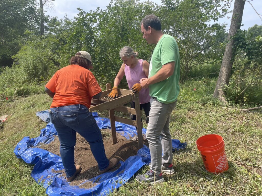 (PHOTO: Dr. Sara Mascia of Historical Perspectives, volunteer Jessica and Aaron Griffiths of The Bird Homestead and Meeting House Conservancy sift through dirt at the William Voris archaeological dig on Monday, July 29, 2024.)