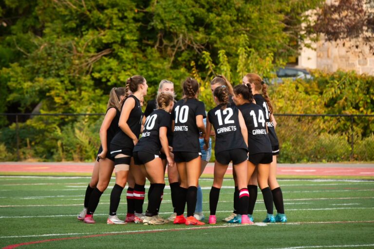 (PHOTO: The Girls Varsity Soccer Team huddles before a game at Nugent Stadium.)