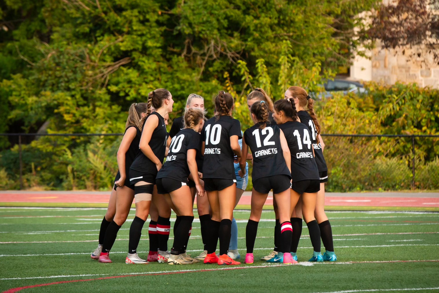 (PHOTO: The Girls Varsity Soccer Team huddles before a game at Nugent Stadium.)