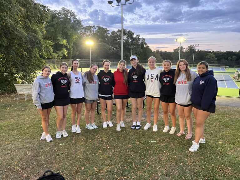 (PHOTO: 11 match players on the Girls Varsity Tennis Team pose under the lights after victory at Harrison High School.)