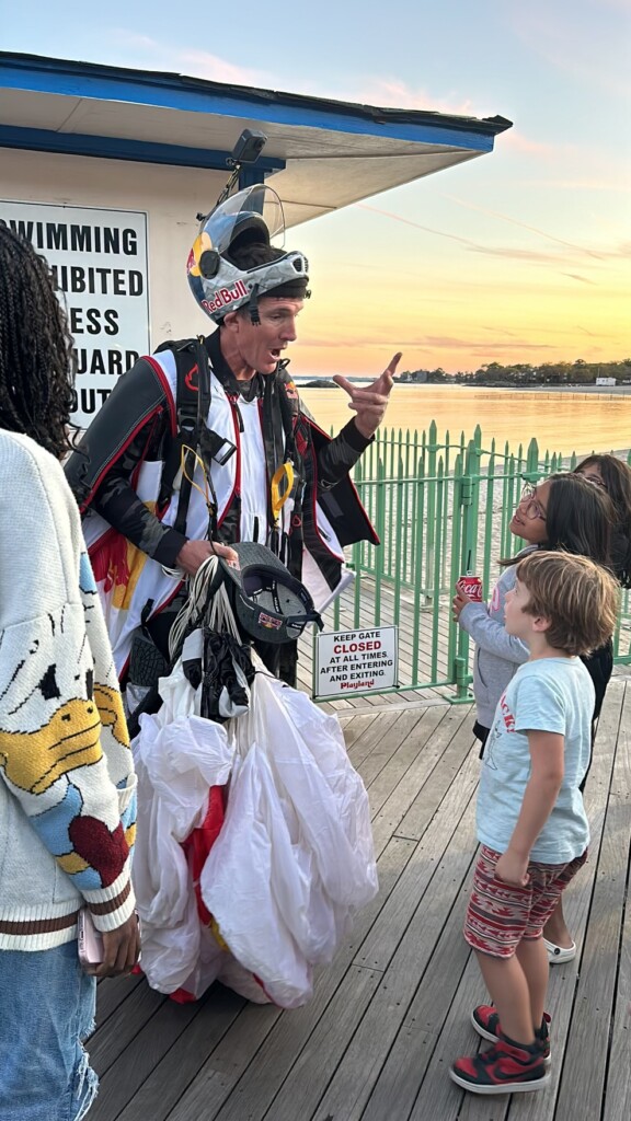 (PHOTO: Jeff Provenzano – 1994 Rye High School grad, professional stuntman and member of the Red Bull Air Force – skydived onto Rye Playland Beach on Saturday, October 12th at 6:00pm. Provenzano on the Playland boardwalk answering questions after his jump. Contributed.)