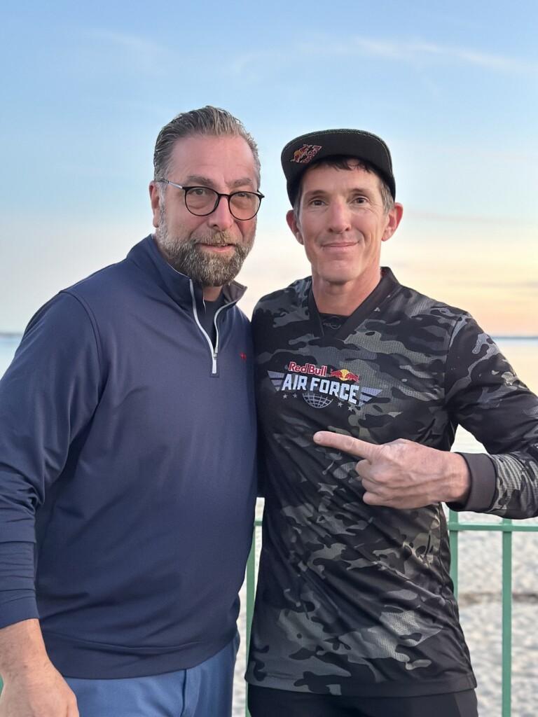 (PHOTO: Jeff Provenzano – 1994 Rye High School grad, professional stuntman and member of the Red Bull Air Force – skydived onto Rye Playland Beach on Saturday, October 12th at 6:00pm. Provenzano (right) with Vincent Corso, owner of the Tiki Bar at Playland.)