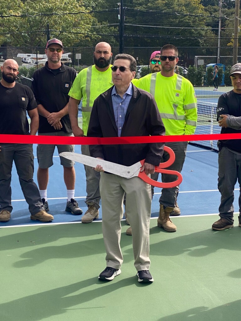 (PHOTO: Mayor Josh Cohn wielding a giant pair of scissors at the official opening of the four new tennis courts at Rye Recreation.)