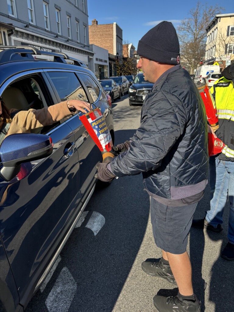 (PHOTO: Rye PD Local 2029 raised $8,472 during the union's annual boot drive on Saturday, December 7, 2024. Fire Fighter Ryan M. Iarocci passes the boot on Purchase Street. Contributed: Local 2029.)