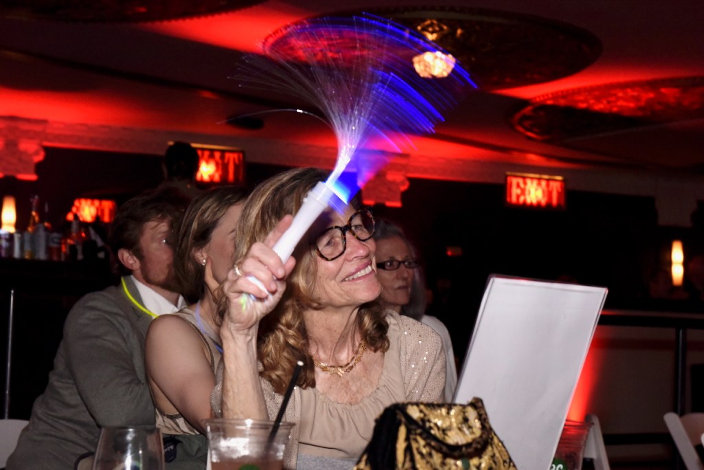 (PHOTO: The Rye Arts Center’s annual benefit Studio 51 on May 15, 2025, raised a record $320,000. Former Rye Record publisher and current City Council candidate Robin Jovanovich, waving her glow wand during the live auction.  Contributed. Credit: Leslye Smith.)