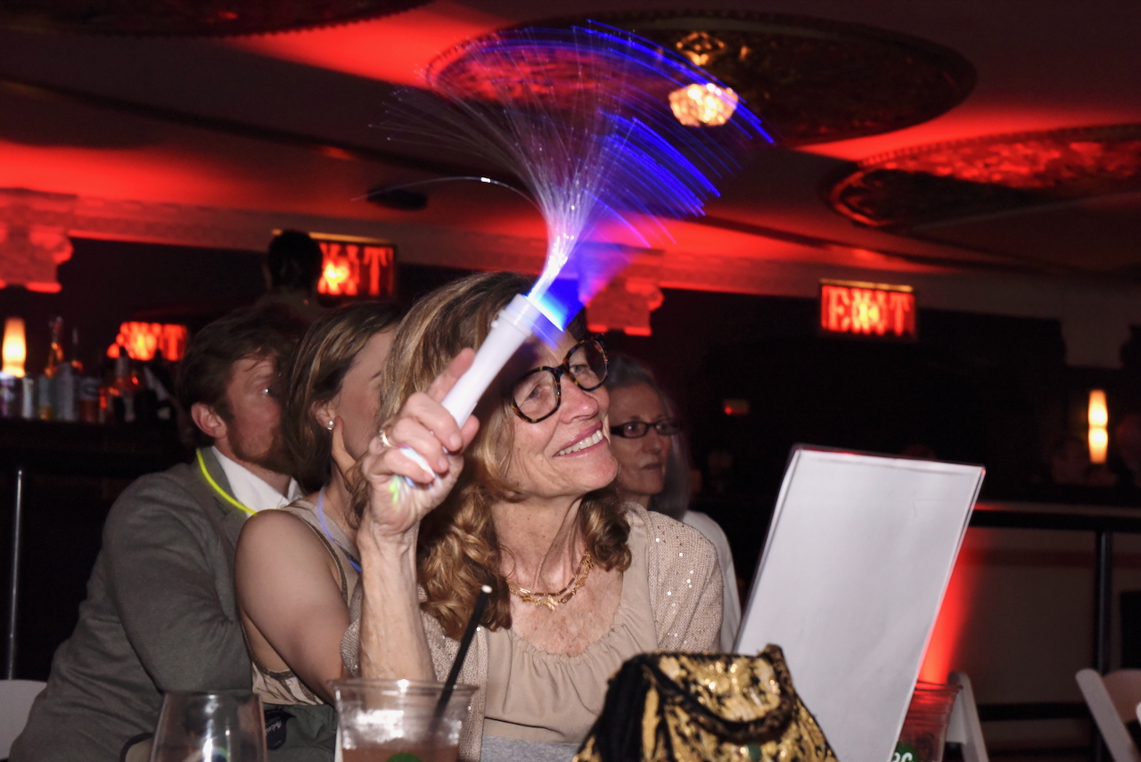 (PHOTO: The Rye Arts Center’s annual benefit Studio 51 on May 15, 2025, raised a record $320,000. Former Rye Record publisher and current City Council candidate Robin Jovanovich, waving her glow wand during the live auction. Contributed. Credit: Leslye Smith.)
