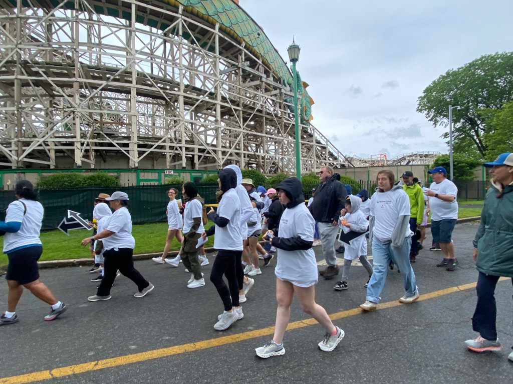 (PHOTO: Supporters walk past Dragon Coaster at Playland Park during the Rye Parkinson’s Project inaugural fundraising walk on May 31, 2025. Credit: Amelie Coghlan.)