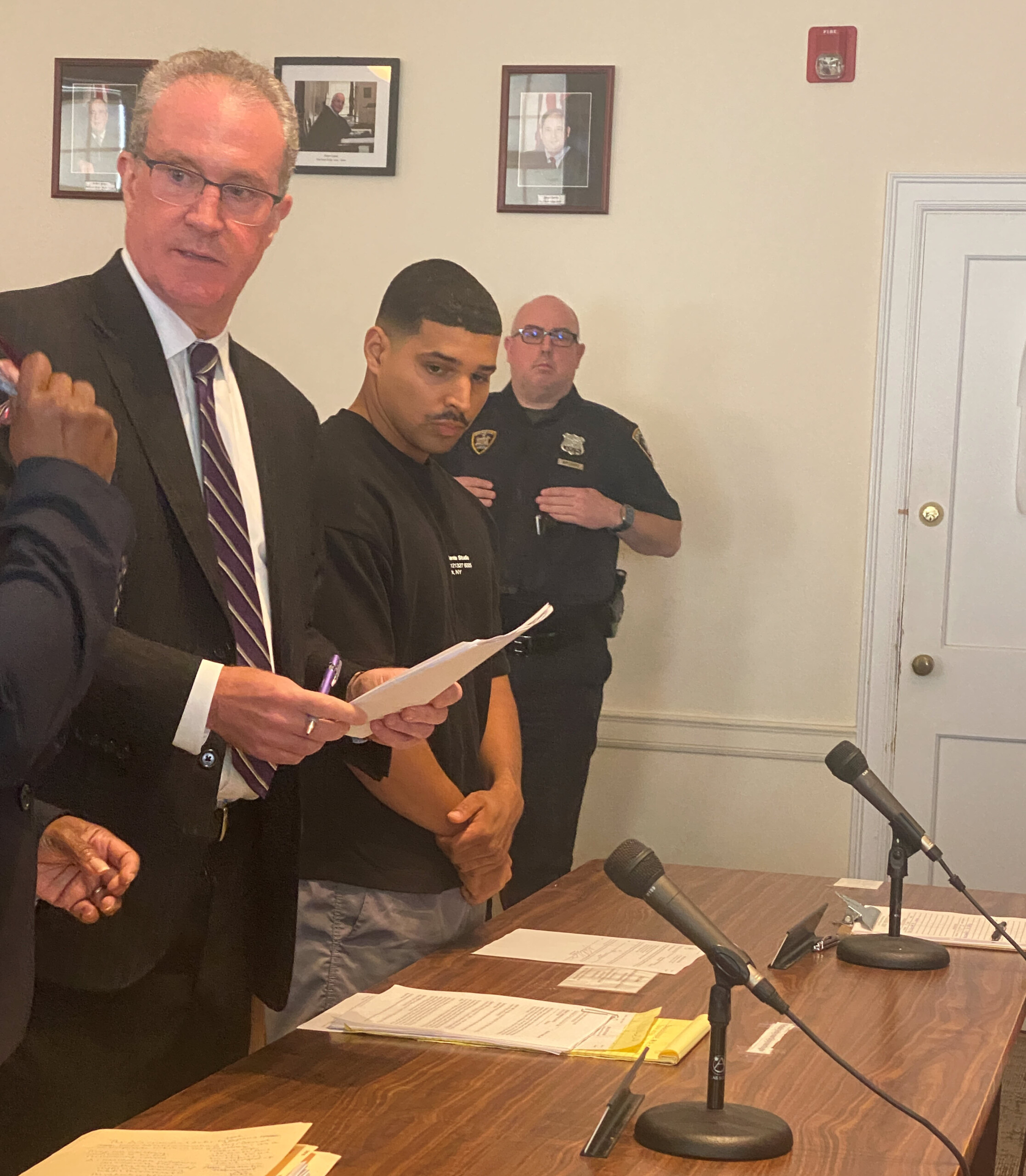 (PHOTO: NYPD officer Yeison Rodriguez-Acosta (standing at the right side of the table), 27, was arraigned on July 17, 2025 before Judge Valerie Livingston in Rye City Court and charged with multiple counts related to stealing more that $85,000 from the accounts of elderly customers of a Rye Brook Wells Fargo bank.)