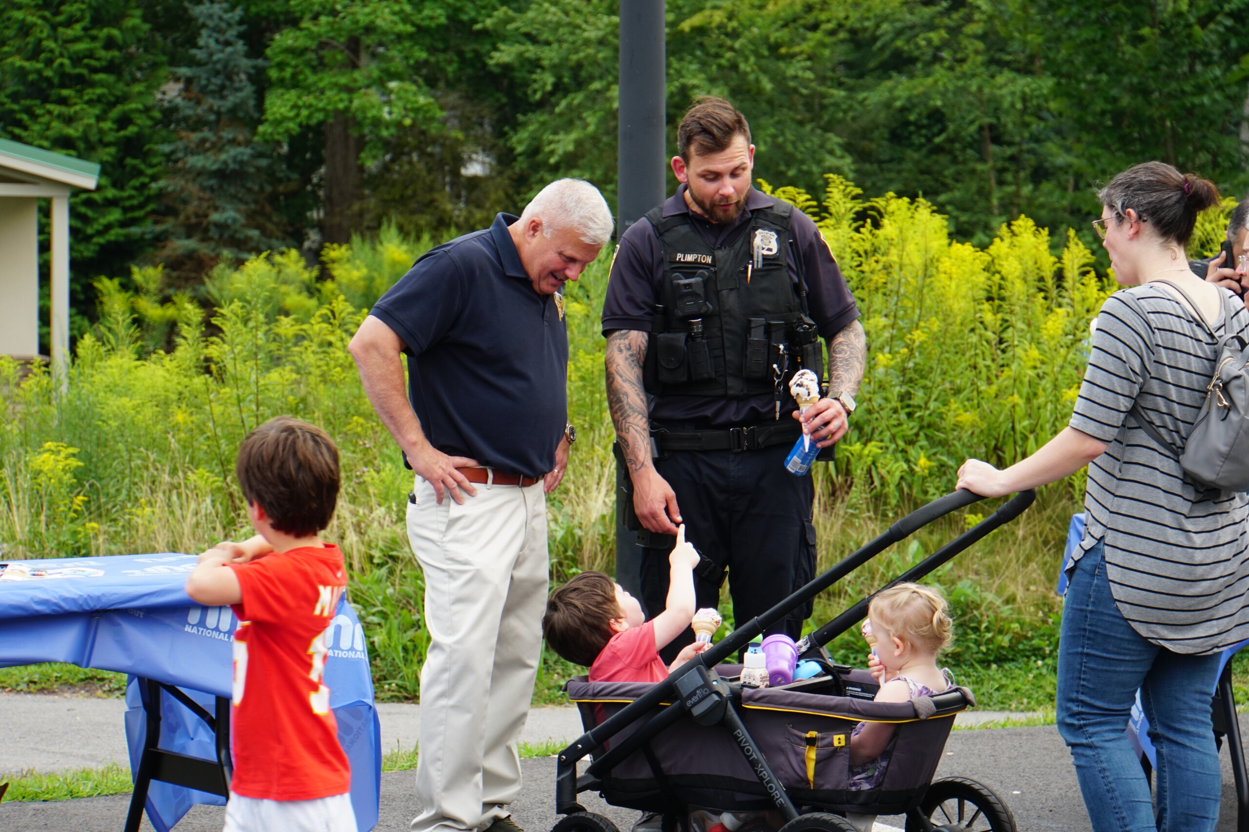 (PHOTO: Rye PD held its third annual National Night Out on August 5, 2025 at Rye Recreation. Public Safety Commissioner Mike Kopy and PO William Plimpton greet future police recruits. Credit: Eli Chopra.)