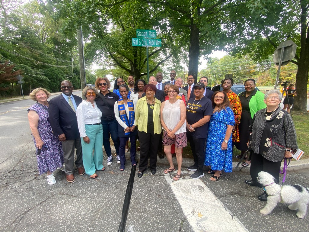 (PHOTO: The Paul & Orial Redd Way street naming at the Rye train station on September 27, 2025. A celebratory group around the new Paul & Orial Redd Way street sign.)