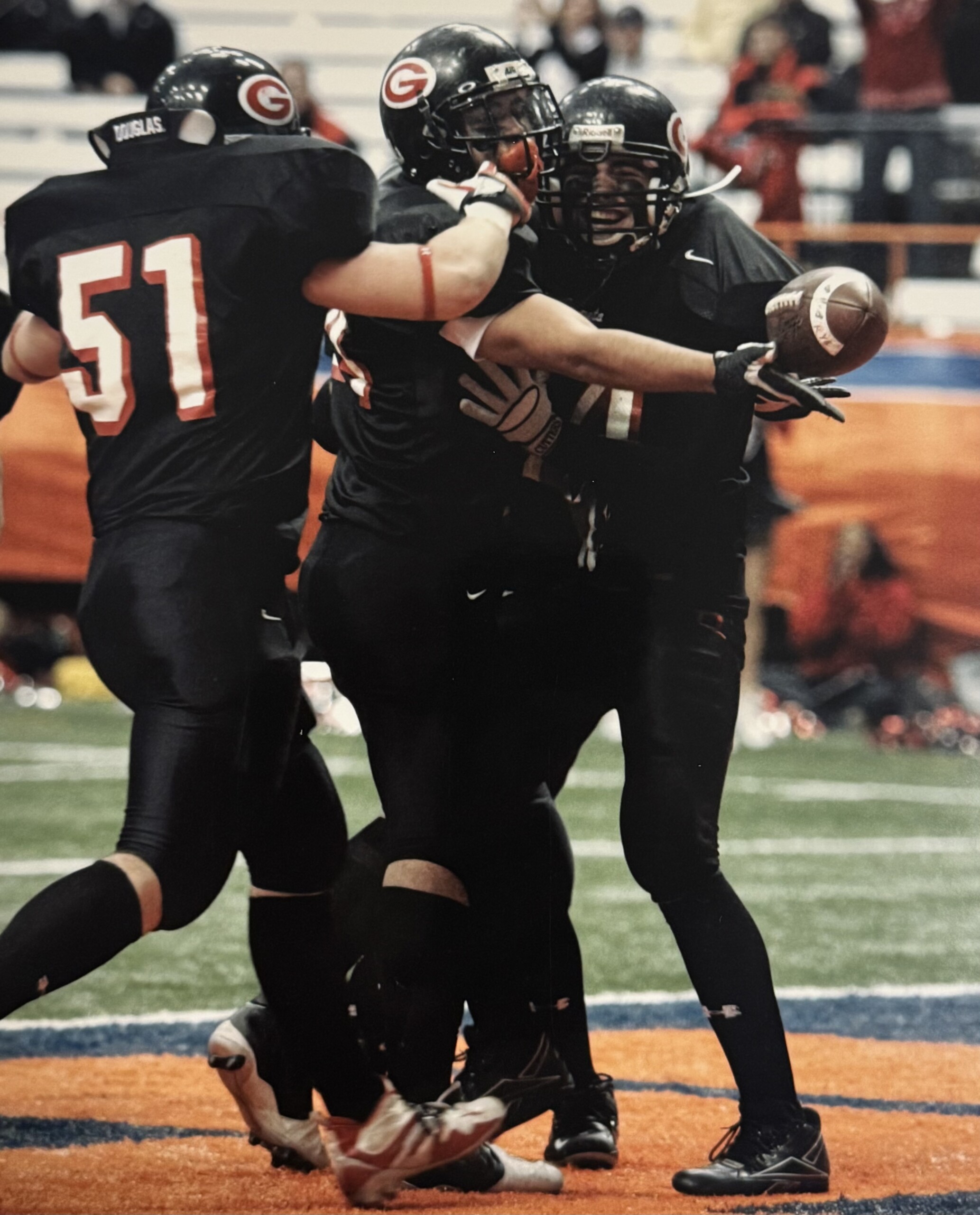 (PHOTO: The Journal News cover after Rye won the State championship in 2005. The photo depicts the first touchdown in the Carrier Dome for the Garnets in their third trip to the field. Players pictured L to R: #51 Jay Adams, #24 Bam Bam (TD scorer), #34 Peter Longo. Contributed.)