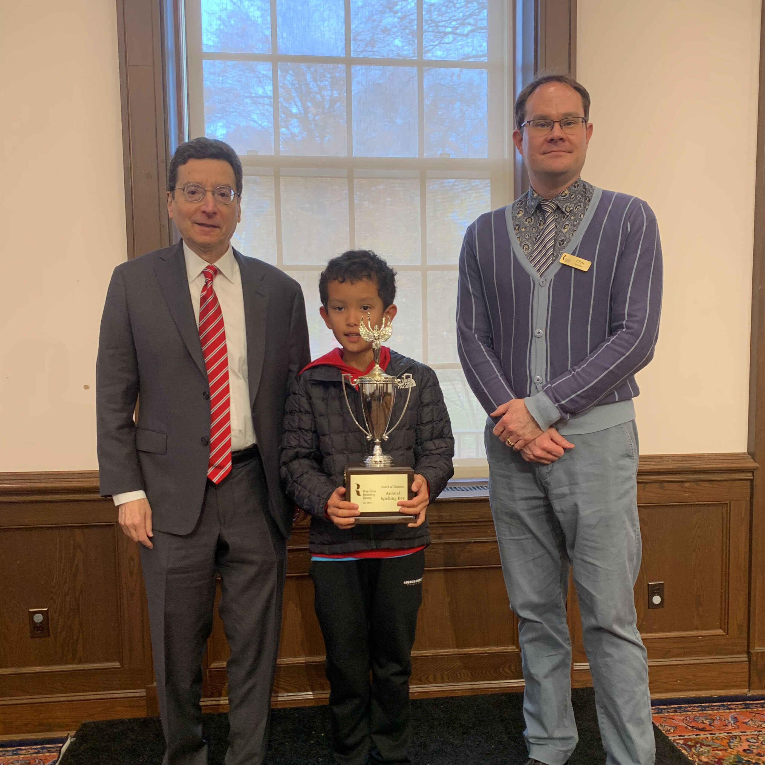(PHOTO: Elementary school winner fifth-grader Camden Paul at the Eighth Annual Rye Free Reading Room Spelling Bee with Rye Mayor Josh Cohn and Rye Free Reading Room Library Director Chris Shoemaker on November 11, 2025. Contributed.)