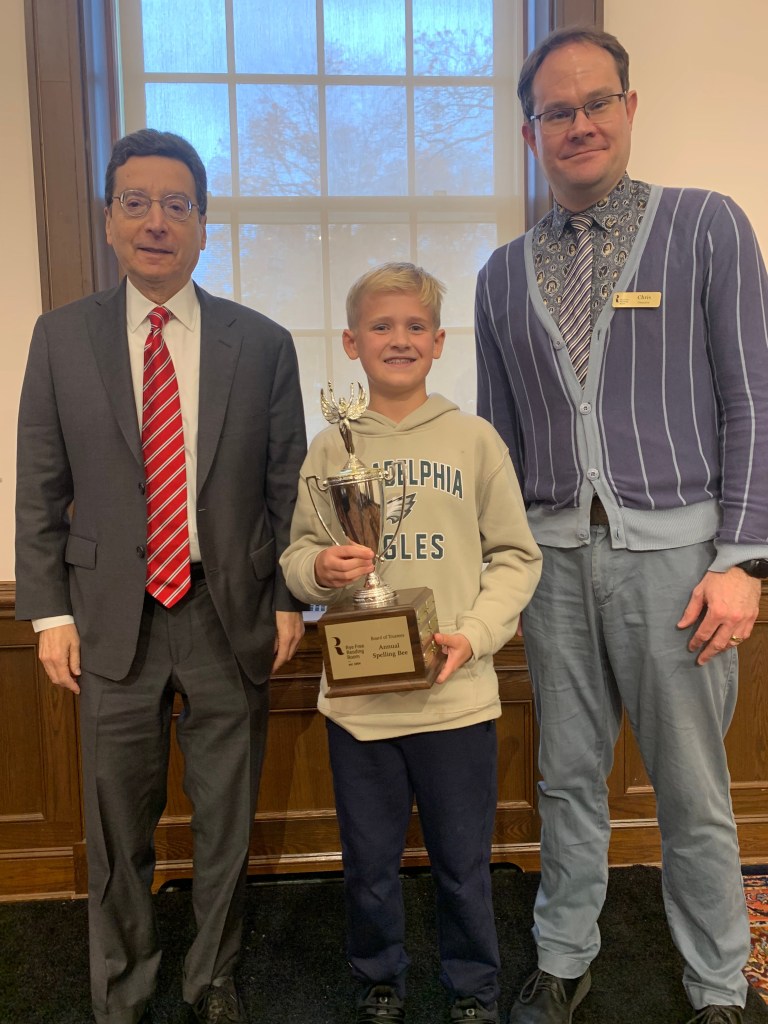 (PHOTO: Middle school winner Owen Beardsley  at the Eighth Annual Rye Free Reading Room Spelling Bee with Rye Mayor Josh Cohn and Rye Free Reading Room Library Director Chris Shoemaker on November 11, 2025. Contributed.)