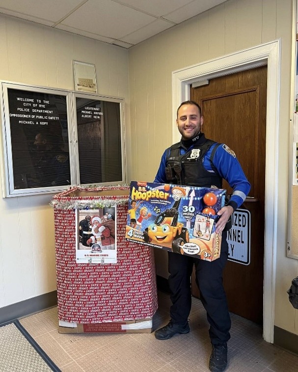 (PHOTO: Rye Police Officer JP Anjo protects the donations for the Rye PBA's annual Toys for Tots drive at Rye Police headquarters. Contributed.)
