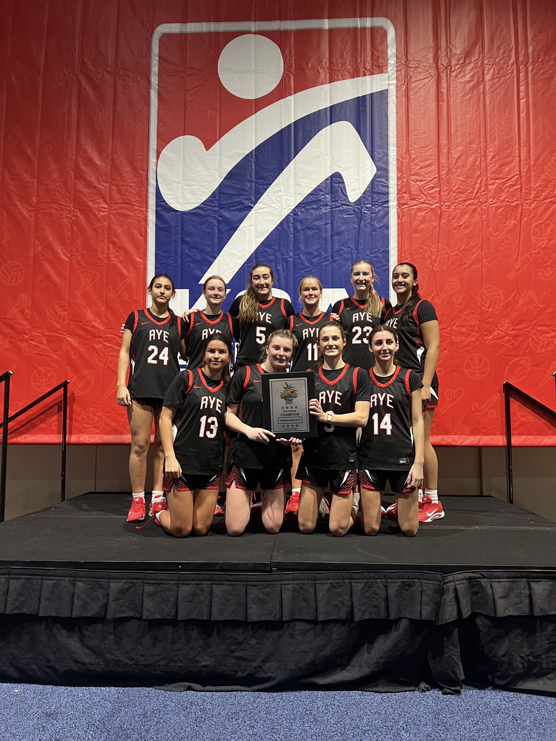 (PHOTO: The 2026 Rye Girls Basketball team with their Orange Bracket Tournament championship trophy from December 30, 2025. Contributed.)