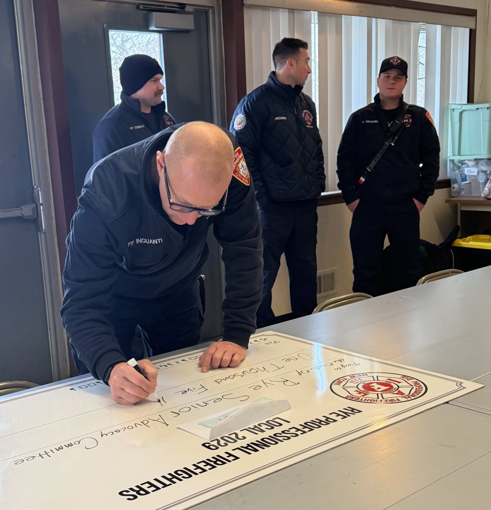 (PHOTO: Rye FD Firefighter and president of 2029 Fundraising Sal Inguanti signs the big check for $1,500 to the Rye Senior Advocacy Committee.)