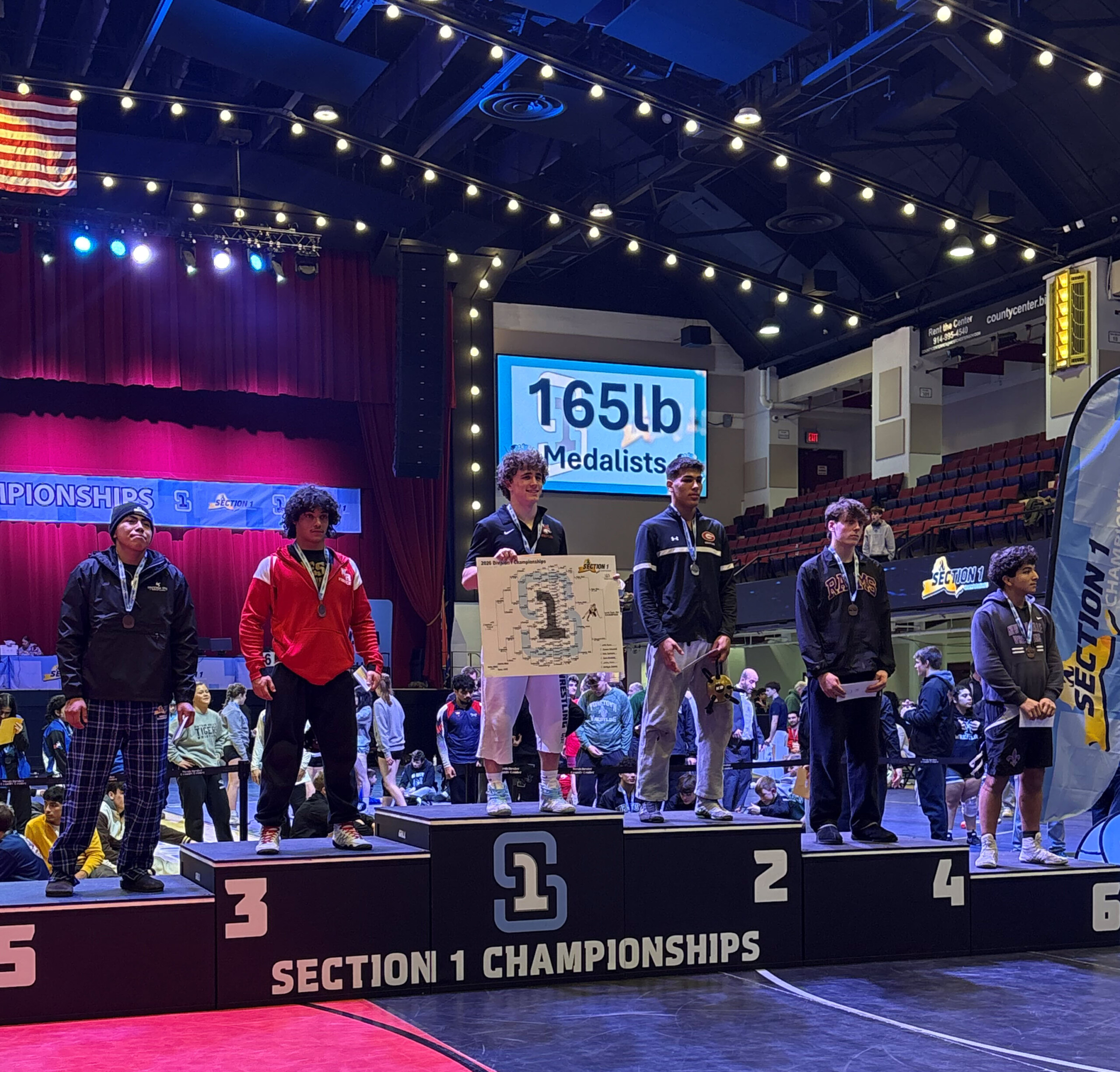 (PHOTO: Rye Wrestling's Jason Gaylord stands on the podium after earning second place in the 165-pound weight class at the Section One Boys Wrestling Championships. Credit: Rye City School District.)