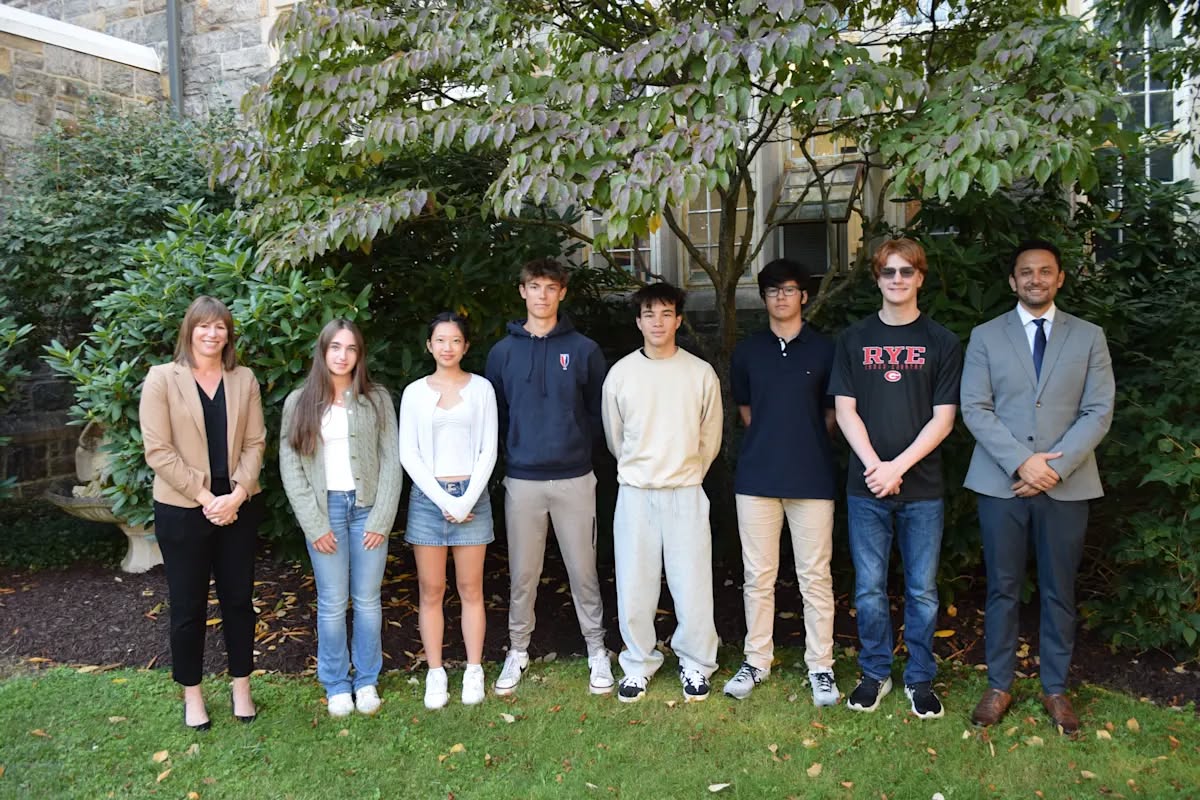 (PHOTO: Rye City School District Superintendent Dr, Tricia Murray; 2026 National Merit Finalists Svetlana (Lana) Andikyan, Grace Wang, Ryan Crozier, Reid Thigpen, Pedro Becker and Jackson Page; and Rye High School Principal Andrew Hara. Contributed.)