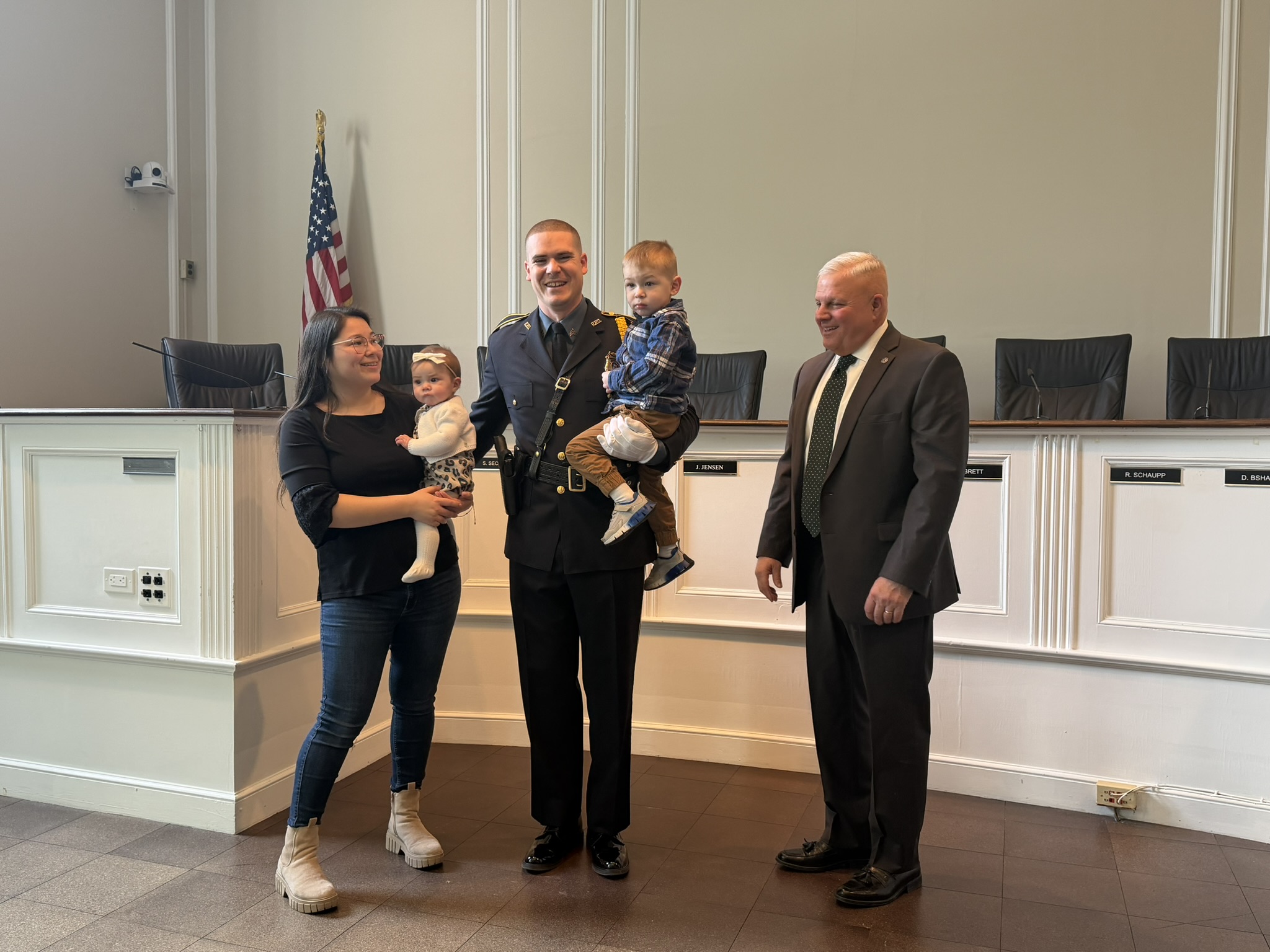 (PHOTO: Sergeant Alex Whalen (center) with with his wife Veronica, baby Carolina, Whalen, son Axel, and Public Safety Commissioner Mike Kopy at Whalen’s promotion at Rye City Hall on March 2, 2026.)