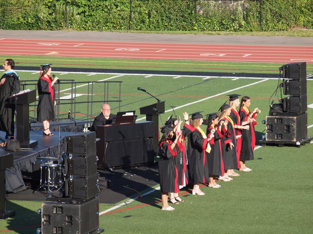 (PHOTO: Eliza Chai was accompanied by ASL performers–Alexandra DellaSalla, Margaret Derman, Alexandra Huen, Phoebe Lee, Charlotte Lincoln, Abigail May, and Melisa Pirinccioglu–in her rendition of the national anthem at the 2026 Rye High School Graduation.)