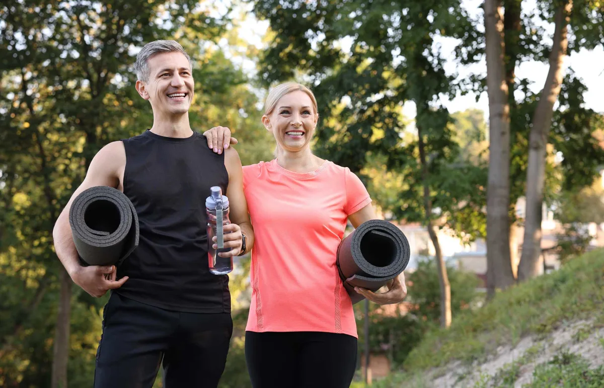 a couple in workout gear holding yoga mats
