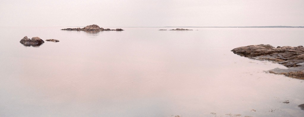 (PHOTO: Quiet on the Sound. Rocks protrude from the surface of the perfectly still Long Island Sound. By Markus Peters.)