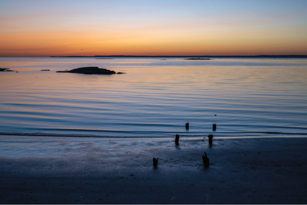(PHOTO: Weathered Posts. Remnants of a dock sitting under a calm sky appear and disappear with the tides. By Stacey Massey, author of First Light, Rye.)