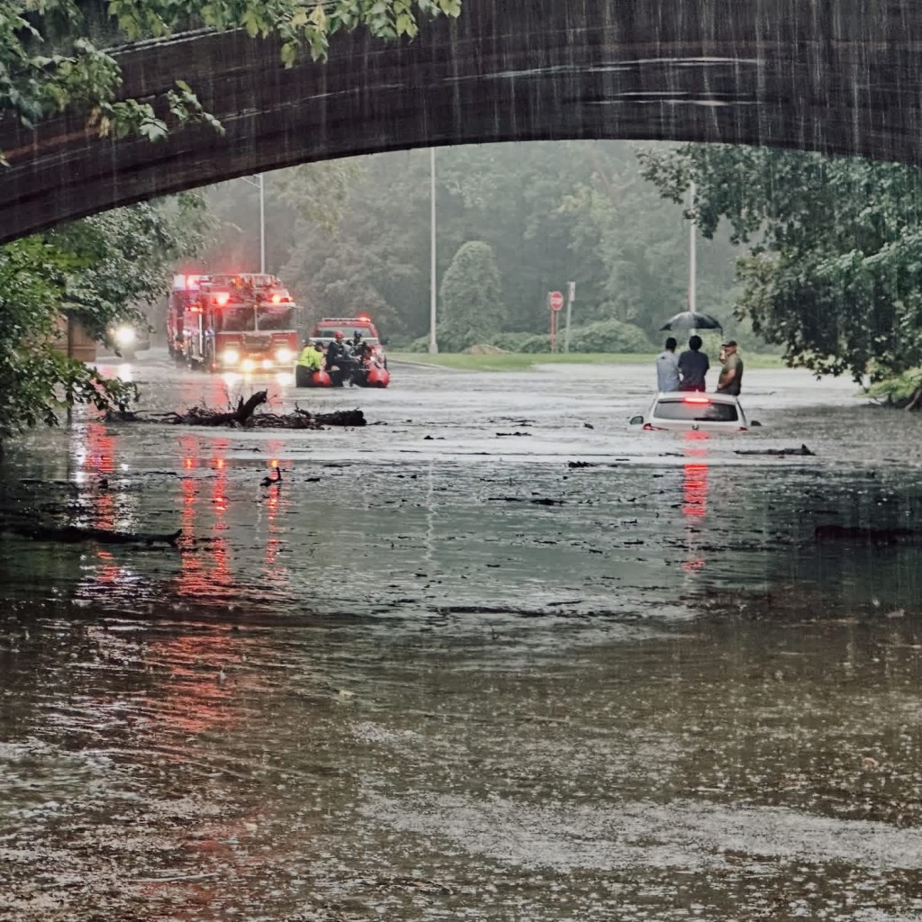 Firefighters rescue people from a car stranded in floodwaters.